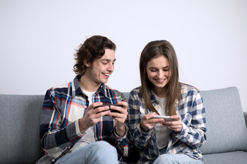 Cheerful couple laughing while using smartphones on sofa