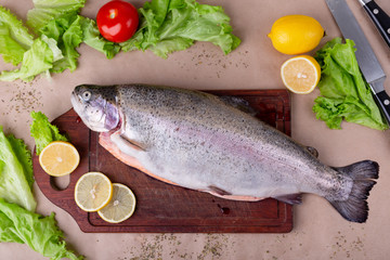 Raw fresh unprepared salmon fish on a wooden board with ingredients for cooking. Lemon, lettuce, tomatoes. Mediterranean cuisine, top view, flat lay.