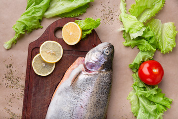 Raw fresh unprepared salmon fish on a wooden board with ingredients for cooking. Lemon, lettuce, tomatoes. Mediterranean cuisine, top view, flat lay.