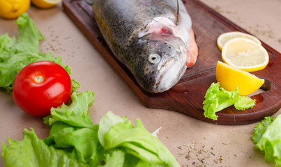 Raw fresh unprepared salmon fish on a wooden board with ingredients for cooking. Lemon, lettuce, tomatoes. Mediterranean cuisine.