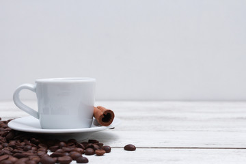White cup of coffee, cinnamon and beans on white wooden table. Coffee shop, spice, espresso, side...