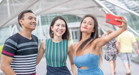 Three asian friends walking along the city taking selfies. Tourism and holiday concept