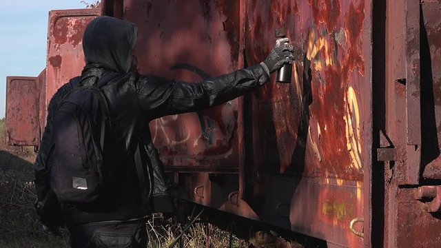 Homeless man spray painting old train wagon with aerosol can