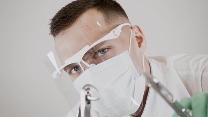 A caucasian male dentist in a mask and glasses releases air bubbles from a syringe with a preparation and holds dental forceps in his hand to remove teeth. Concept of dental care and dental treatment.