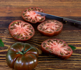 schwarze tomate mit tomatenscheiben und messer auf einem holztisch