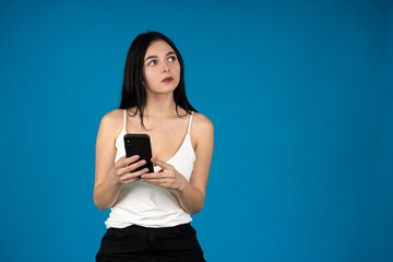 Pensive brunette girl with smartphone looking away isolated on blue background