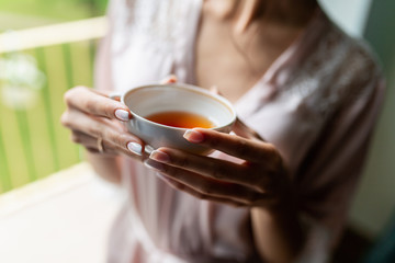 Close-up of a beautiful Cup of tea with a drawing in the hands of a girl in a soft pink robe. Cup...