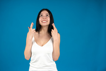 Front view of smiling girl with crossed fingers isolated on blue background