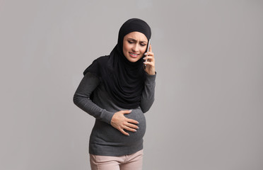 Pregnant arabic woman suffering from abdominal pain and calling to doctor