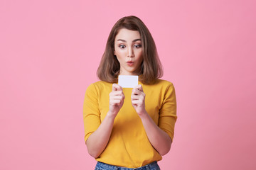 excited young woman in yellow shirt showing credit card isolated over pink background.