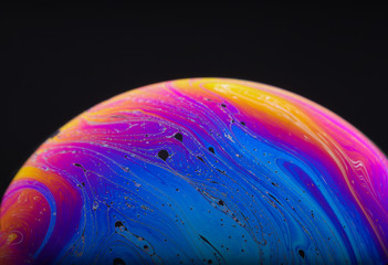 Close up macro photograph of the psychedelic rainbow of colors mixing and swirling in a soap bubble to look like a fantasy galaxy or planet isolated against a black background