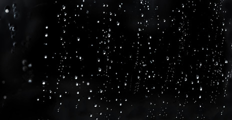 Falling Rain water drops on a black dramatic window glass. Autumn  depression background. Rain pattern.
