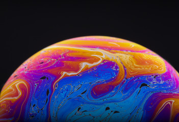 Close up macro photograph of the psychedelic rainbow of colors mixing and swirling in a soap bubble to look like a fantasy galaxy or planet isolated against a black background
