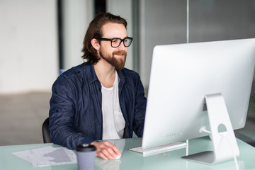 Young businessman working in office, sitting at desk, looking at computer screen