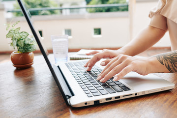 Horizontal shot of hands of unrecognizable young woman working on laptop in modern office