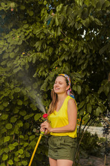 Beautiful young smiling woman watering plants in her garden with a garden hose. hobby concept.