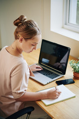 Vertical High Angle shot of young woman sitting at table working on something iin modern office