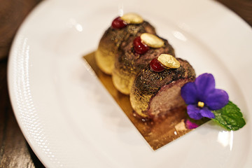 Haute cuisine or high kitchen food concept. Chocolate coated duck liver pate decorated with edible candied crystallized violet flower. Exquisite exclusive meal.