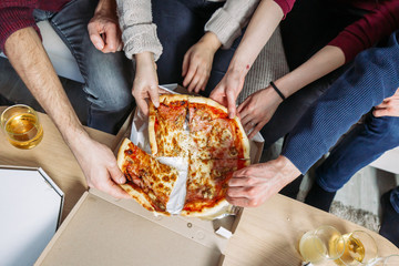 Male and female hands grabbing pieces of pizza. Movie night at home with friends