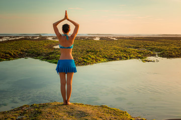 Yoga pose. Woman standing on the sand, practicing yoga. Young woman raising arms with namaste mudra...