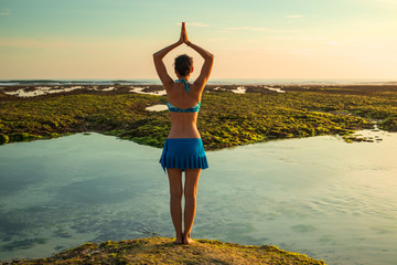 Yoga pose. Woman standing on the sand, practicing yoga. Young woman raising arms with namaste mudra...