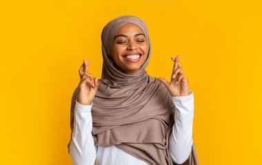 Positive afro muslim woman in hijab making wish with crossed fingers