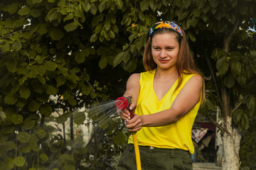 young pretty girl having fun in the garden watering plants with a hose. Smiling while taking a...