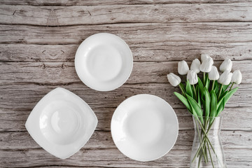 White empty plates with a bunch of tulips in a glass jar on old wooden background of a table. Top view with copy space for text