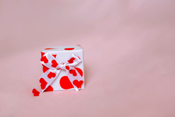A gift box with a heart pattern on a pink background, with a small red heart on the background, for copy space.