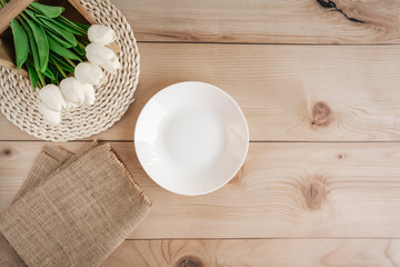 Minimally decorated table with tulip flowers, white plate and decorations on wooden table. Top view. Table setting concept.