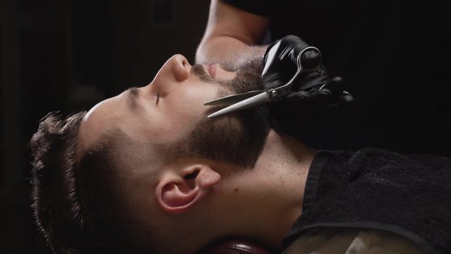 Professional hairdresser shaving man's beard using razor