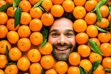 Man with ripe oranges, concept for food industry. Face of grimacing man in oranges or mandarins area 
