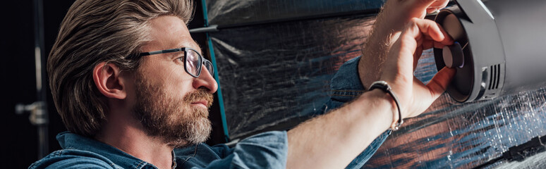 panoramic shot of bearded art director touching reflector in photo studio