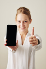 Vertical medium studio portrait of happy Caucasian woman demonstrating new gadget with thumb up