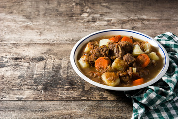 Irish beef stew with carrots and potatoes on wooden table. Copy space