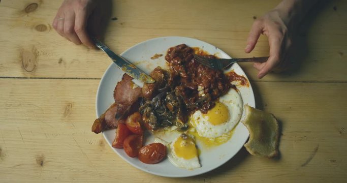 Hands of a young woman eating traditional english breakfast