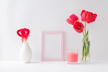 Home interior with decor elements. Mockup with a pink frame, red tulips in a vase on a light background