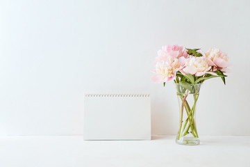 Mockup with a blank desk calendar and pink peonies in a vase on a white background