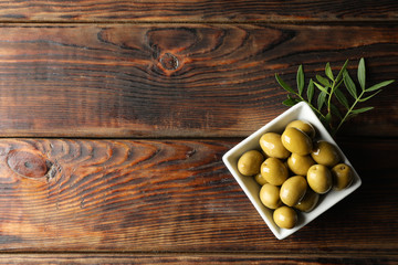 Square bowl with olives and leaves on wooden background, top view