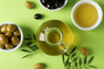 Olives, bottle and bowl with olive oil on green background, top view and close up