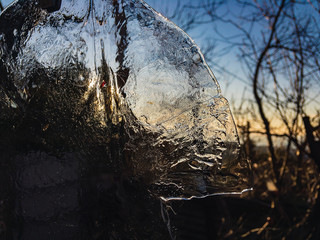 View through transparent ice to a winter landscape without snow with blue sky and sunlight.