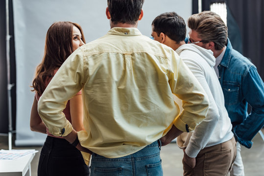 Back View Of Man Standing With Hands On Hips Near Coworkers In Photo Studio