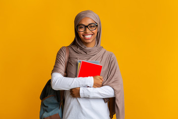 Happy black muslim student girl in hijab with backpack and notepads