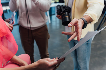 cropped view of photographer pointing with finger at paper near coworkers