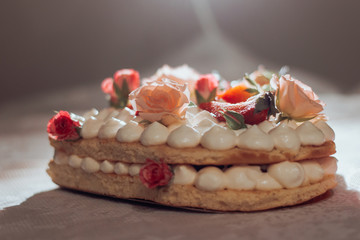 White cream sponge cake with roses and strawberries on top against the light. Side view