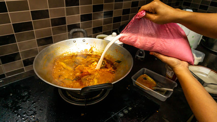Hand put some coconut milk into the fish head curry in the metal wok to make the food more tasty.