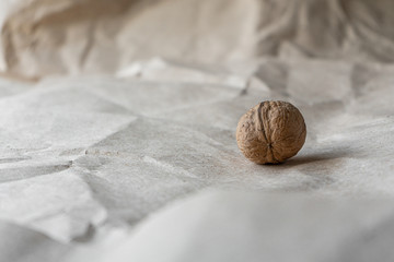 Side view. One inshell walnut on old crumpled kraft paper, brown background, warm beige pattern