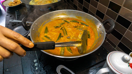 Hand mixed some coconut milk into the fish head curry in the metal wok using spatula.