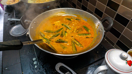 Hand mixed some coconut milk into the fish head curry in the metal wok using spatula.