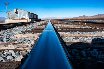Railroad tracks, at ground level, with warehouse and mountains in background